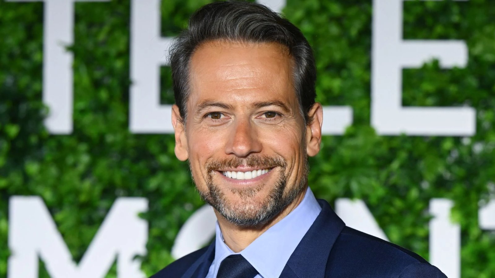 Ioan Gruffudd smiling on the red carpet at a film premiere in London, wearing a navy suit and light blue shirt.